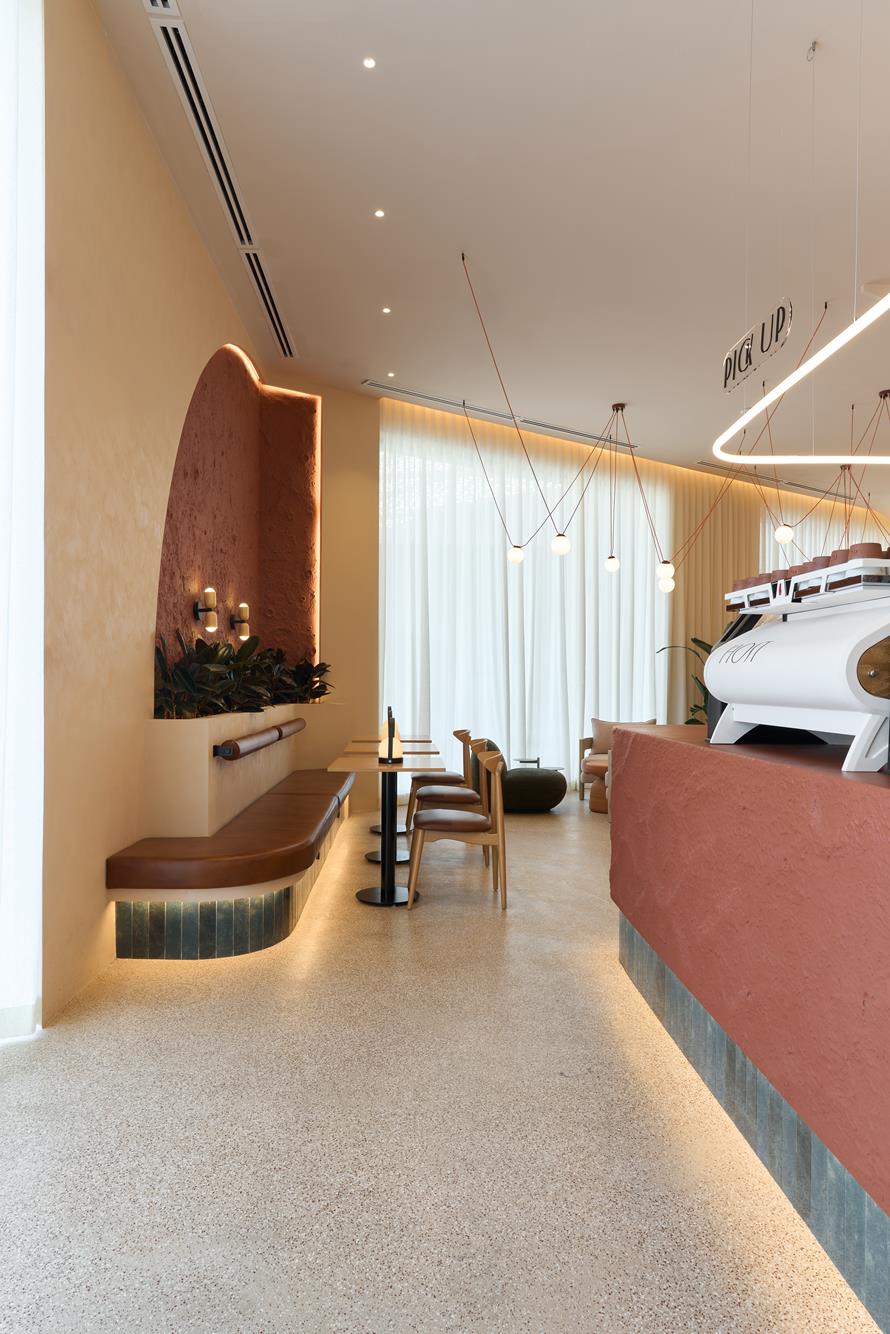The café’s long side, terrazzo underfoot and a terracotta counter carrying the espresso machine