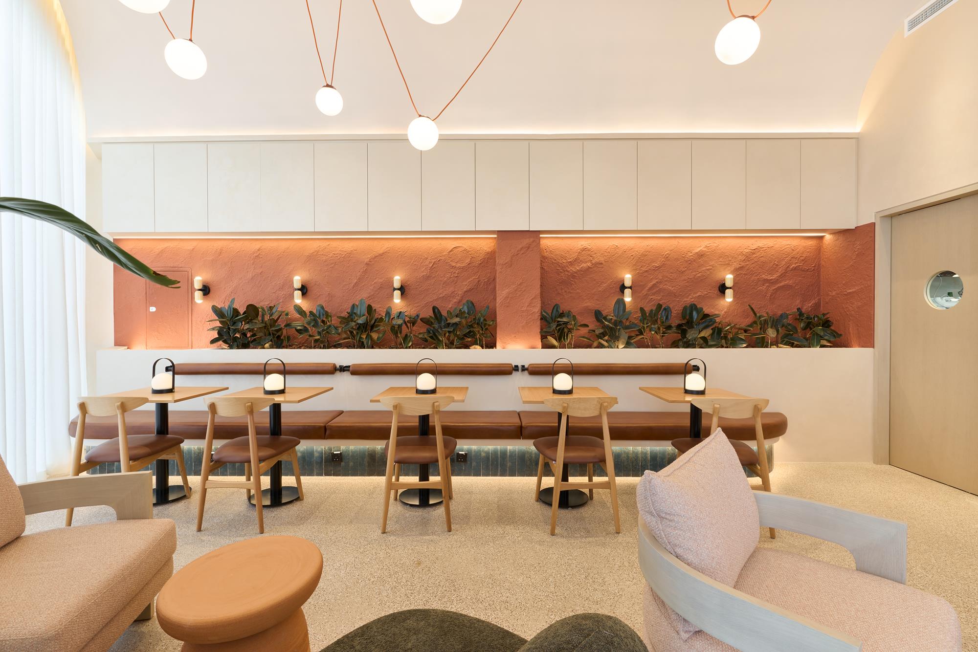 A banquette run under a lit planting niche, portable lamps set along the tables