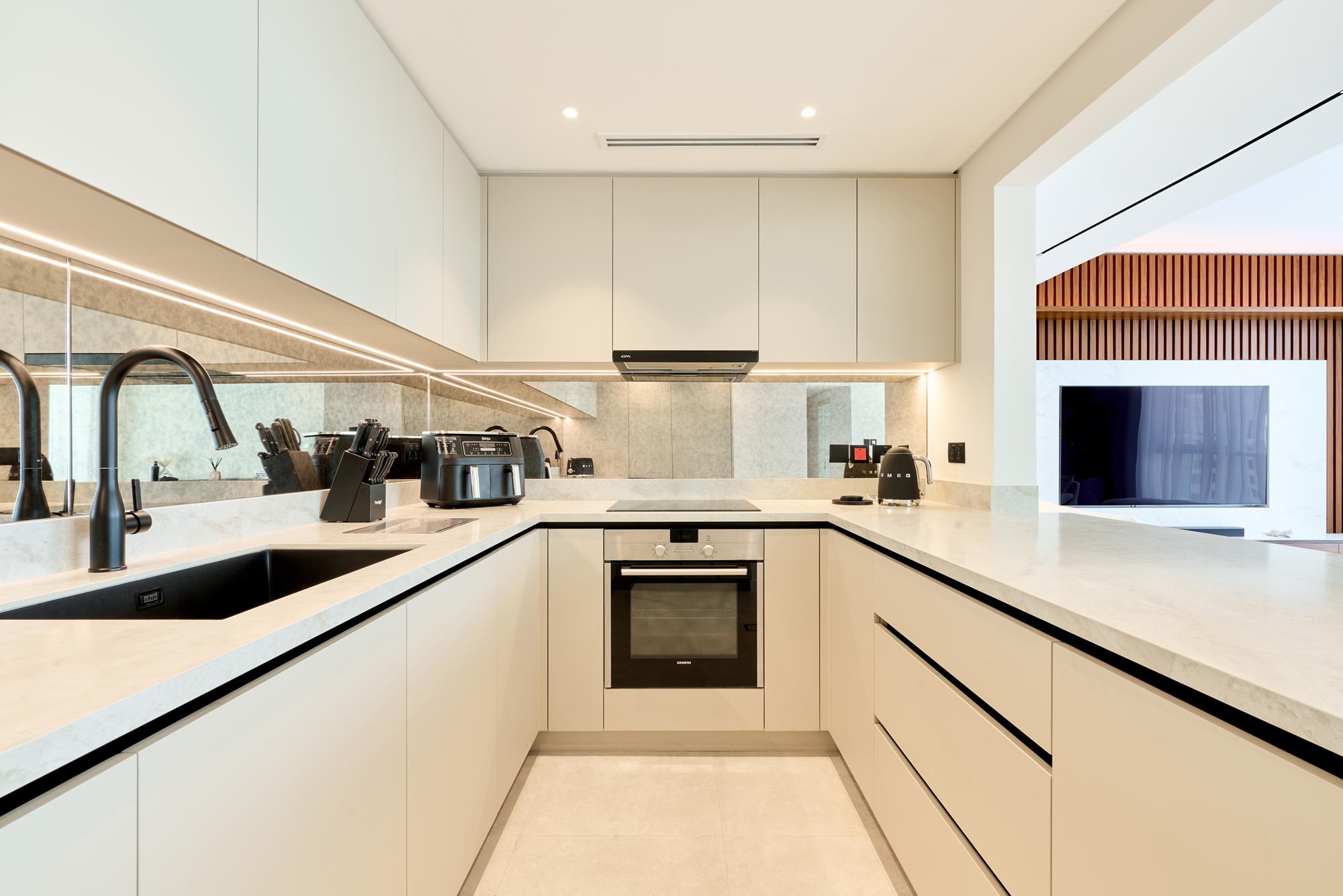 A galley kitchen in pale stone and handleless joinery, lit along every shadow gap