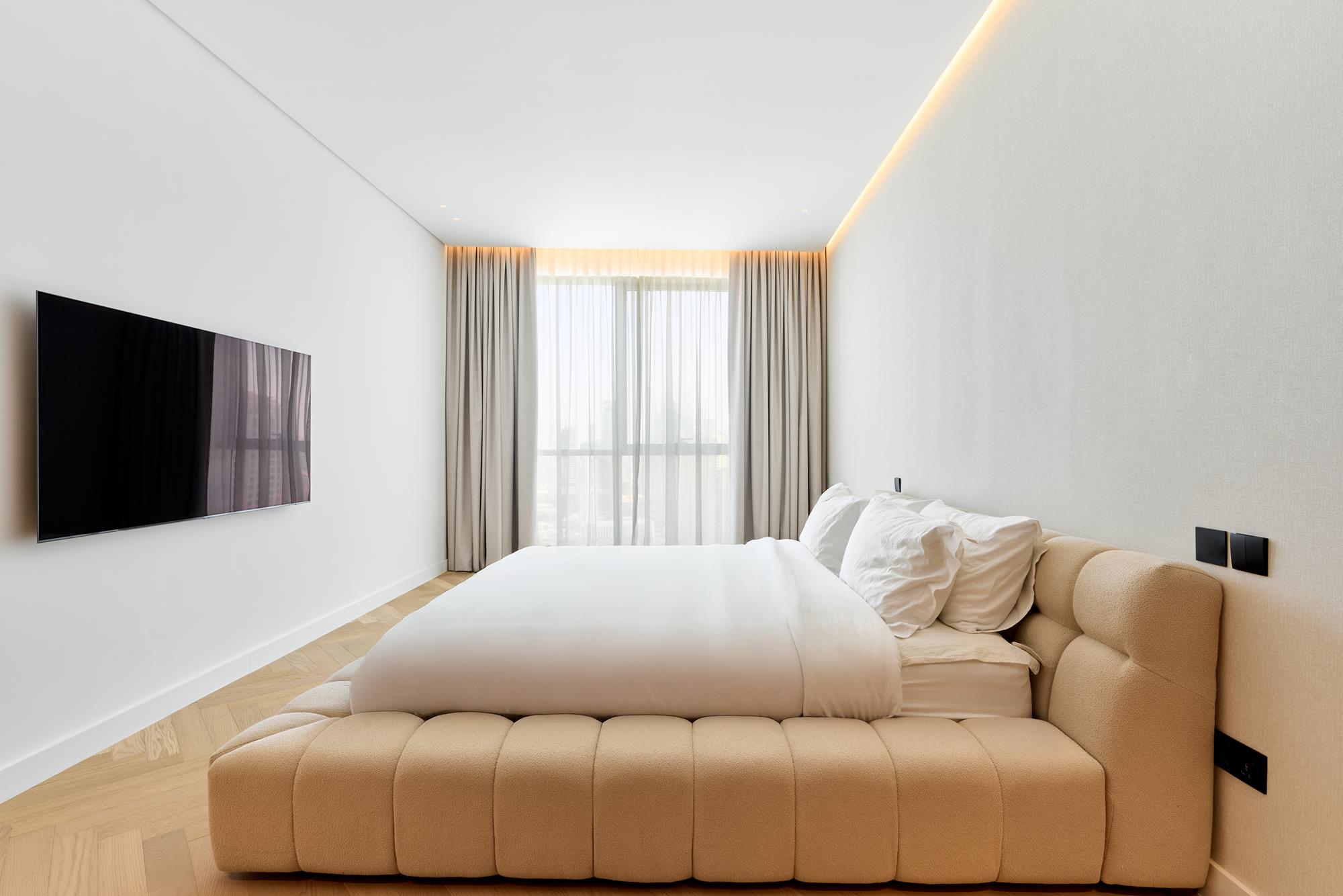 A bedroom pared back to a bouclé bed, a cove of warm light and a curtained window