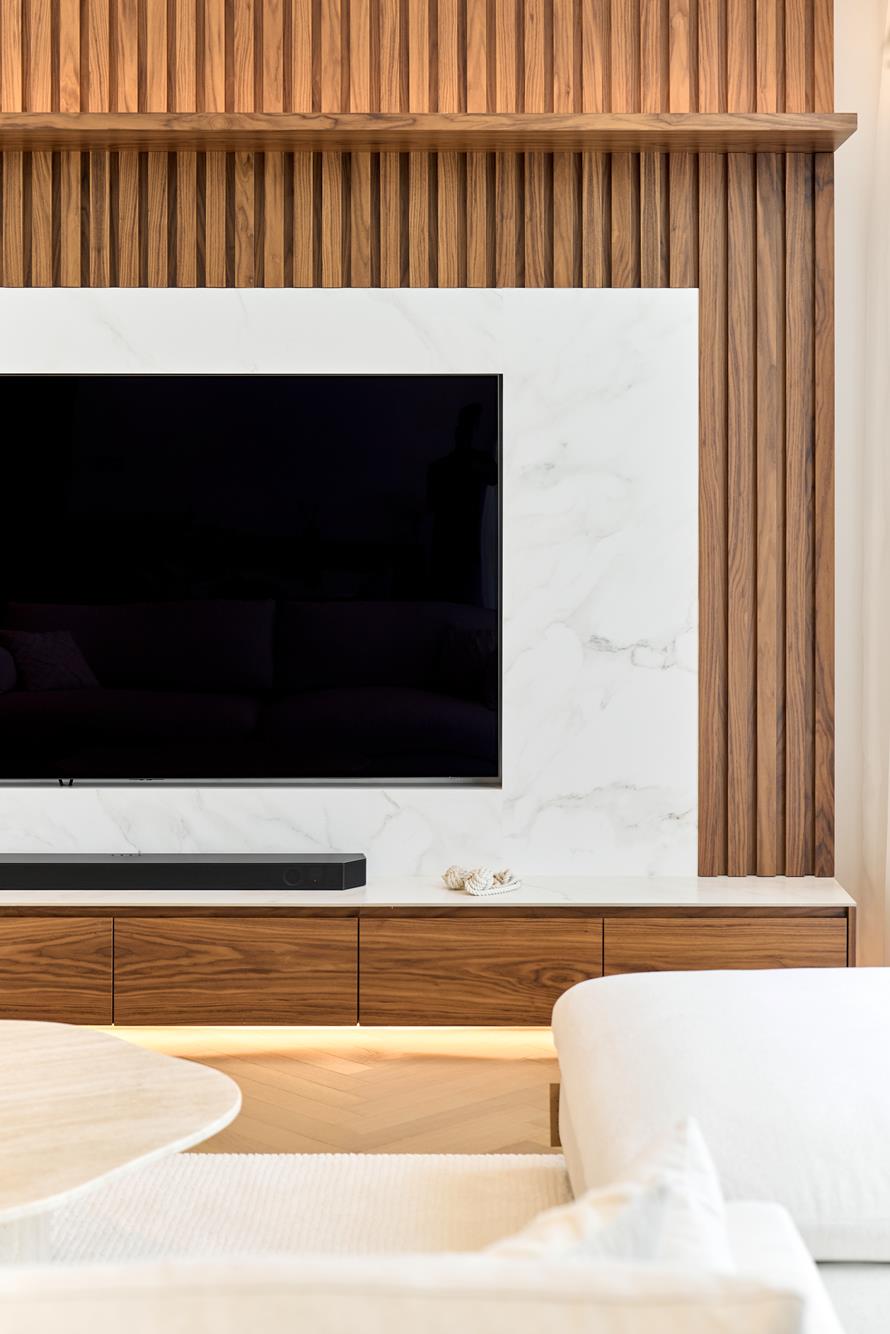 A walnut-slatted media wall inset with a panel of white marble