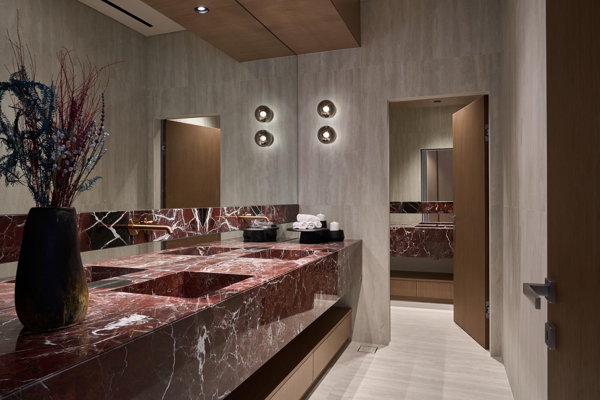 Burgundy marble vanity beneath limestone walls and warm light