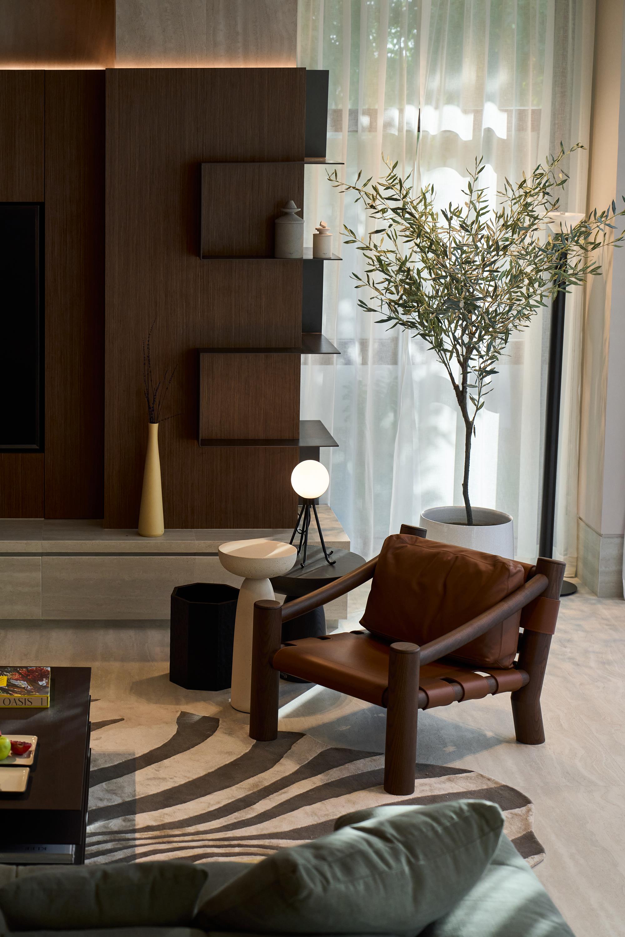 A living corner with leather sling chair, olive tree and walnut shelving