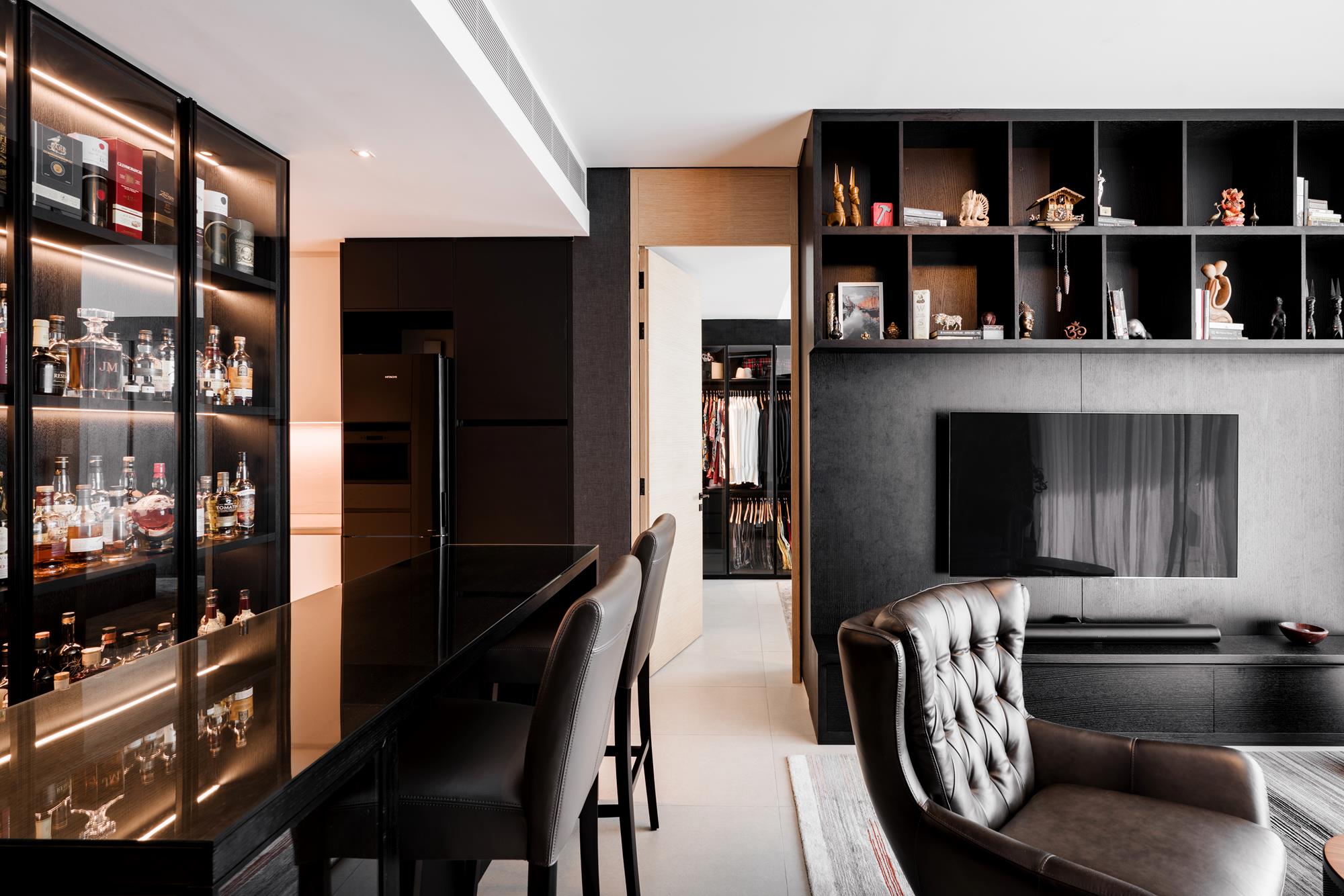 An open plan of bar, kitchen and media wall resolved in a single dark language