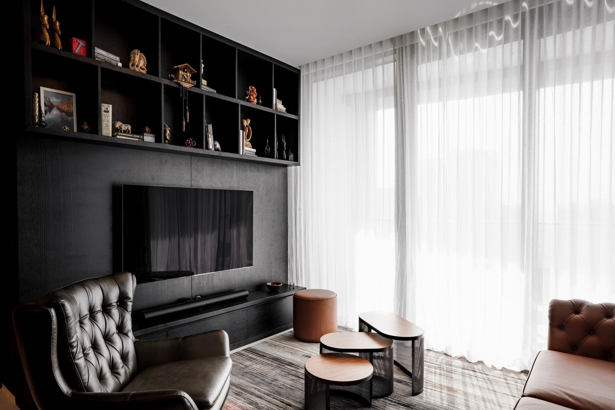 A living room in blackened oak joinery behind sheer daylight curtains