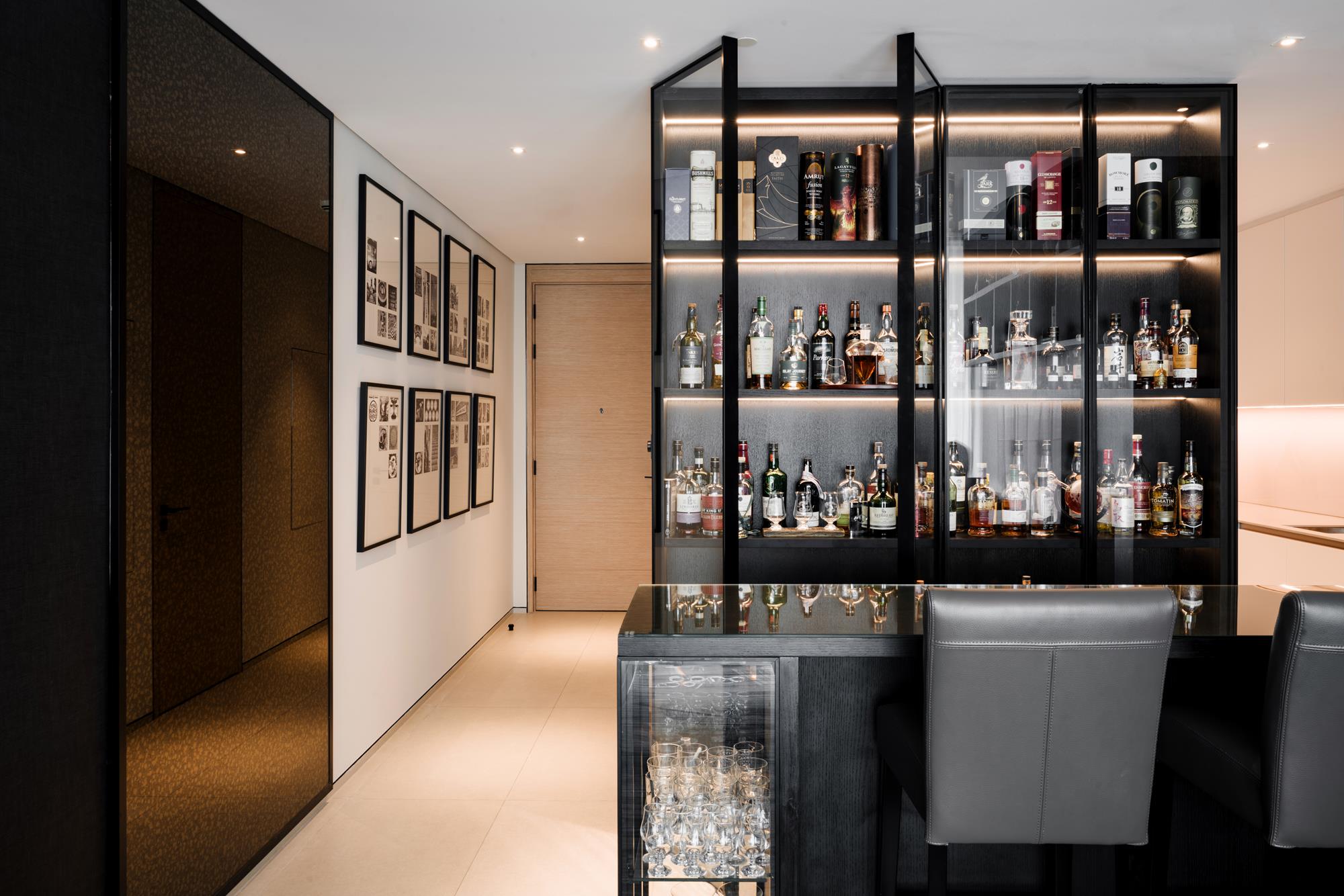 The entry corridor with a gallery hang facing a glazed, back-lit bar wall