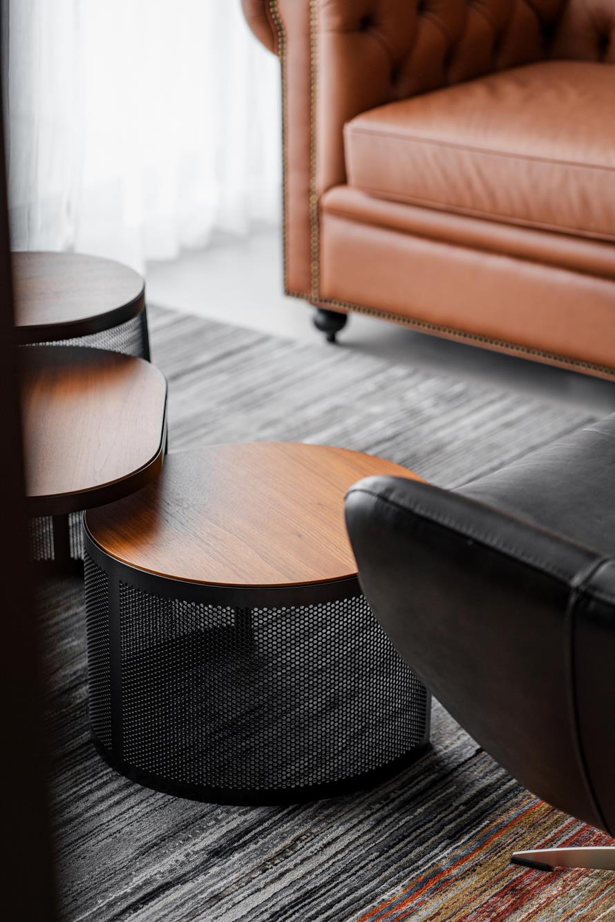 Nesting walnut and mesh side tables between a tan leather Chesterfield and a black lounge chair