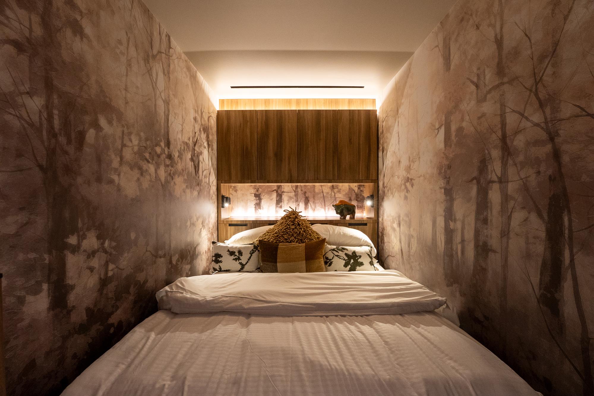 A cocooning bedroom wrapped in soft forest-mural walls