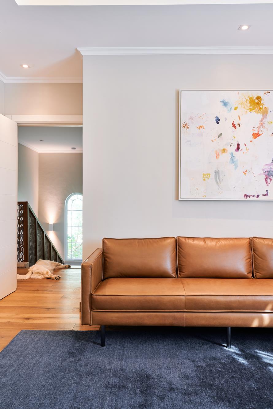 A tan leather sofa below an abstract canvas, the stair hall beyond