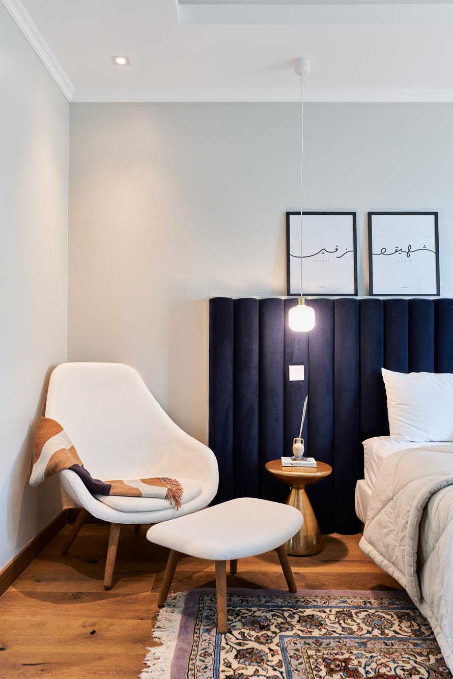 A bedroom corner with fluted navy headboard, reading chair and Arabic calligraphy prints