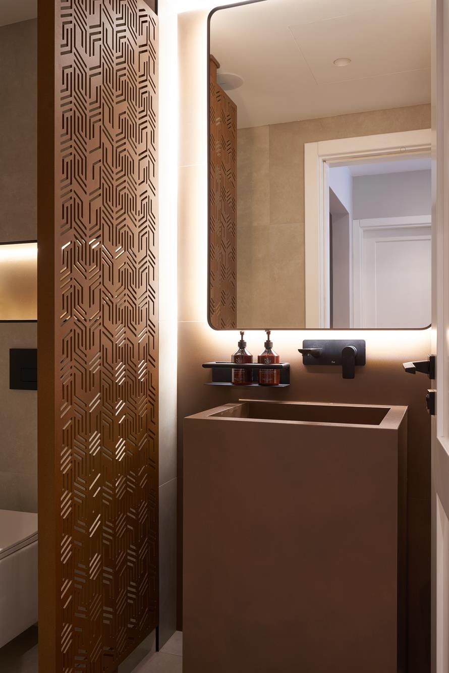 A cloakroom where a lit moucharabieh panel meets a monolithic basin
