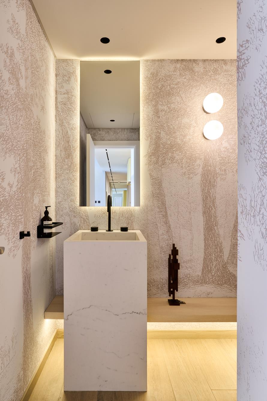 A guest cloakroom lined in forest-drawn wallpaper around a marble monolith basin