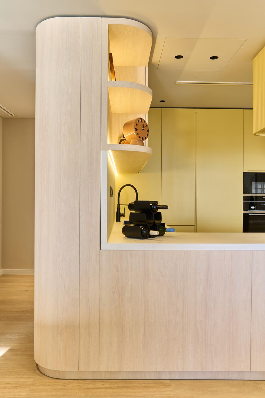 A curved ash joinery pier opening onto the yellow kitchen behind