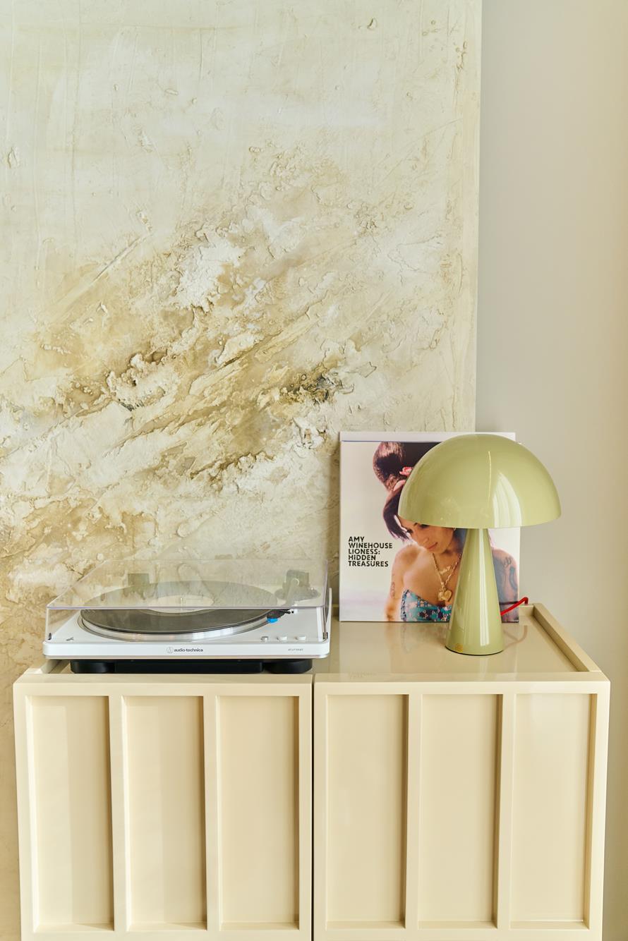 A turntable and a soft-green lamp against a hand-plastered textured panel